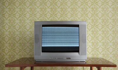 Old TV on the nightstand on the background of the wallpaper. Noise on the screen.