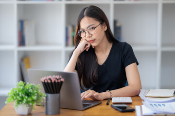 Freelance Asian businessperson, businesswoman sitting at desk thinking, staring at laptop screen, analyze and consider the work in front of her.