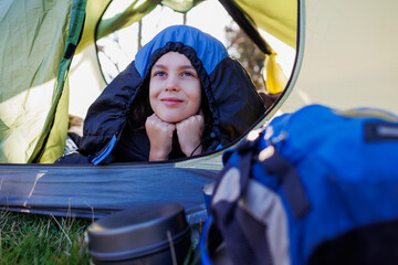 camping and trekking with children. happy smiling child lies in a tent covered with a sleeping bag....
