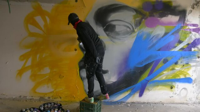 Graffiti artist spraying a colorful portrait mural on a wall
