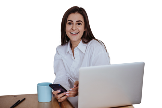 Amazed brunette young woman in white shirt sitting at desk with laptop toothy smiling looks at camera happily. Beautiful Hispanic girl holds phone, remote working against transparent background. - Powered by Adobe