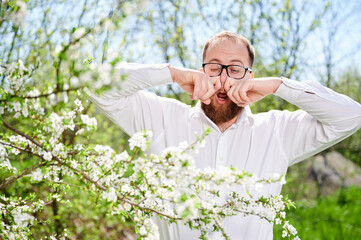 Man allergic suffering from seasonal allergy at spring in blossoming garden. Close up bearded man...