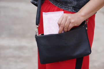 Closeup woman holds sanitary pad for menstruation to put into bag before going out. Concept, female's hygienic product for period's day. Menstrual pain on the day of period. Woman healthcare. Monthly 