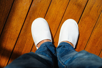 A man wearing white hotel disposable slippers with wooden floor pattern background. Hotel, travel...