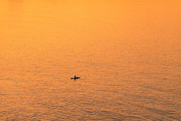 Adventurous people on a stand up paddle board is paddling during a bright and vibrant sunrise