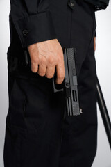Anonymous man in black uniform carrying short-barrelled handgun, firearm, lowered down. Crop view of policeman with black pistol, holding forefinger on trigger, isolated on white. Concept of weapon.