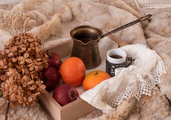 Fototapeta na wymiar Coffee set, fruits, dried hydrangea flower on a wooden tray on the background of a fur blanket.