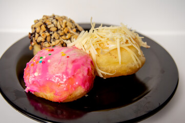 three mini donuts with delicious flavors on a black plate on a white background