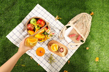 Picnic basket with fruits, flowers, lipsticks and book on the white checkered mat in the green park...