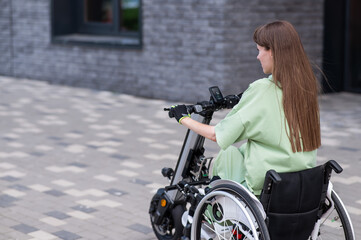 A woman in a wheelchair with an assistive device for manual control. Electric handbike. 