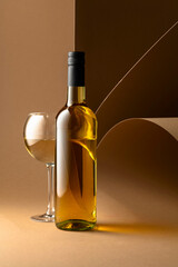 Bottle and glass of white wine on a beige background.