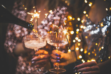 The girls pour champagne into round glasses. Women in a sparkling dress. Christmas garland