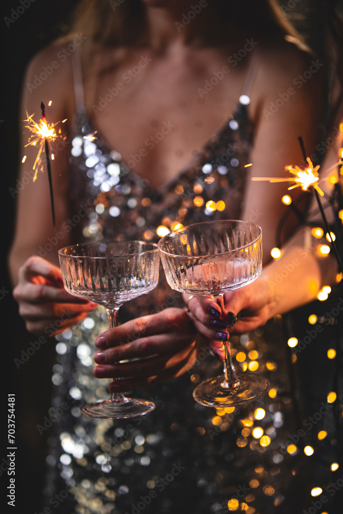 Wall mural the girls pour champagne into round glasses. women in a sparkling dress. christmas garland