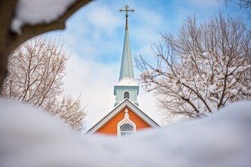 steeple of a small church peeking above snow-laden trees