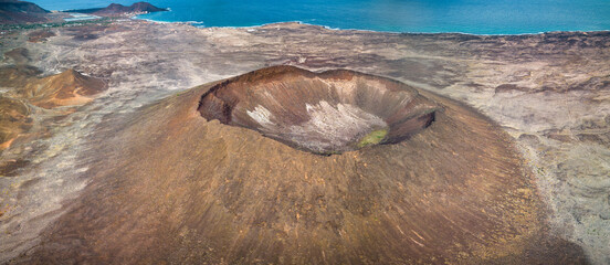 .Aerial view of the Viana Volcano on São Vicente, Cape Verde, showcasing the distinct crater with layered earthen textures against a coastal backdrop