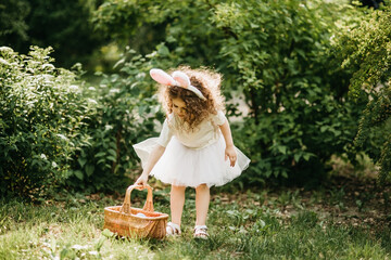 Obraz premium Easter egg hunt. Girl child Wearing Bunny Ears Running To Pick Up Egg In Garden. Easter tradition. Baby with basket full of colorful eggs.