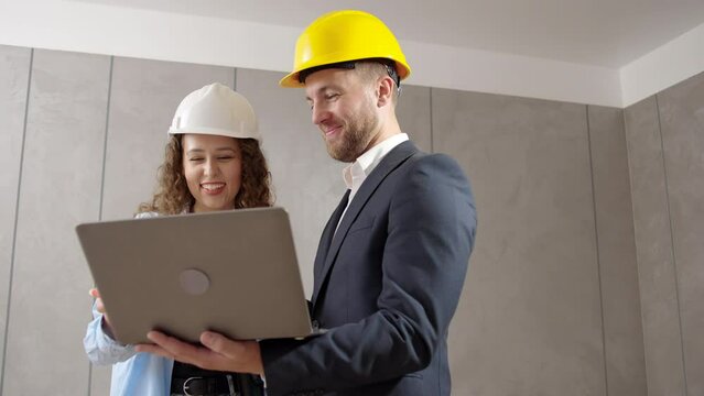 young man and woman in helmet choose room design on computer during an indoor renovation
