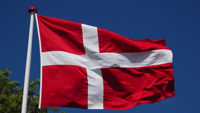 Denmark. National country flag on blue sky background. Danish flag flutters in the wind against the background of the blue sky. in the wind against the background of the blue sky.