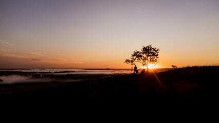 The silhouette of a photographer with a tripod on top of a mountain at dawn