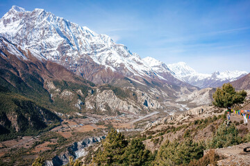 A breathtaking view of the Annapurna range with its rugged terrain and towering peaks, overlooking a serene valley dotted with traditional Nepali homes