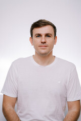Young serious man in a white T-shirt on a gray background. Portrait
