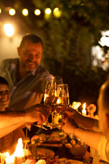 HAppy friends saying cheers and showing their champagne glasses full of sparkling wine to each other whilst enjoying an outdoor wedding party on a backyard restaurant at sunset