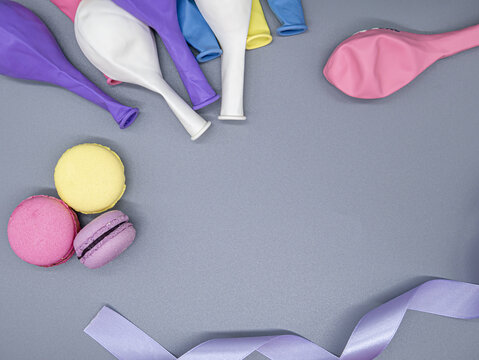 Uninflated colored balloons, lilac lentana and macrone cake for a birthday lie on a gray background, space for text