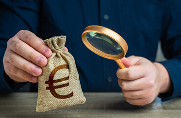 A man examines a euro money bag with a magnifying glass. Checking the origin of capital. Anti money...
