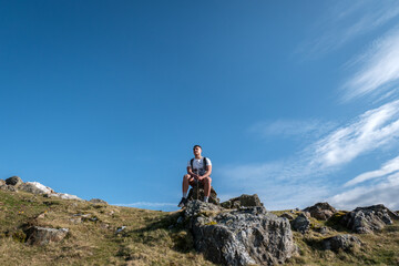 Jovem turista no alto da montanha, sentado sobre uma rocha a apreciar a paisagem enquanto descansa