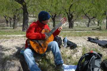 Musician playing classical guitar, outdoors wearing a beanie, red fleece jacket and jeans