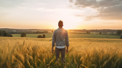 Naklejka na ściany i meble rear view carefree freedom successful male standing confident looking at the end of skyline in the grass field meadow landscape summertime sunset moment nature background