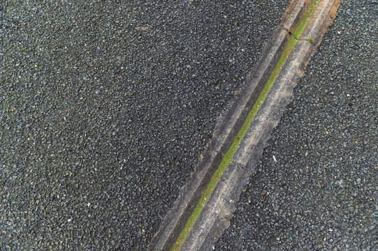 imagen detalle textura suelo asfaltado con una regata para conducir el agua, llena de musgo verde 