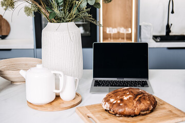 Homemade Bread on Kitchen Table with Laptop. Freshly baked homemade bread on a cutting board beside a laptop, depicting a cozy home baking scene possibly following an online recipe.