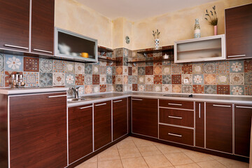 Fototapeta na wymiar Brown furniture in the kitchen with mosaic colorful tiles on the walls