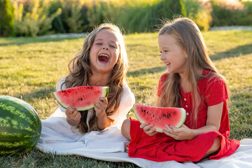 Two laughing merrily little girls two sisters eating watermelon on the lawn. picnic in the park. happy childhood. space for text. High quality photo