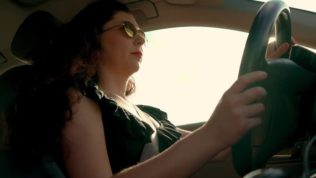 Woman in sunglasses driving car with hands on steering wheel to control vehicle at sunset. Adult female having safety ride in vehicle. Young traveling travelling by SUV