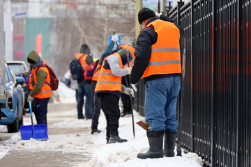 Workers with shovels and crowbars cleaning sidewalk, snow and melting ice removal in winter city