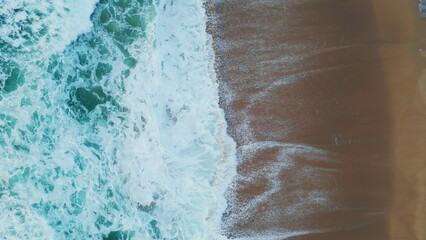 Blue sea water crashing of sandy beach in slow motion. Aerial view ocean waves.