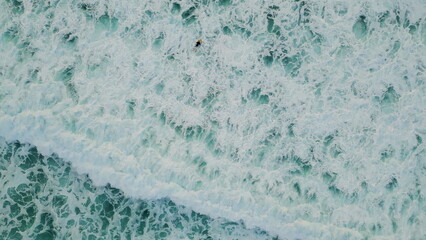 Aerial foaming sea water splashing rolling in slow motion. Surfer swimming ocean