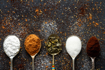 Spoons with icing sugar, green tea, coffee and cocoa on black background sprinkled with sugar, coffee, cocoa powder.