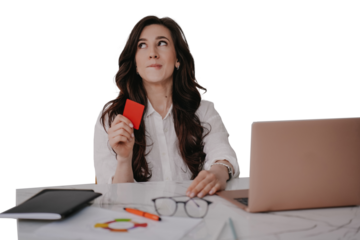 young woman sitting at desk with laptop holding credit card with dreamy face against transparent background, thinking about new purchase. Remote employe received salary.