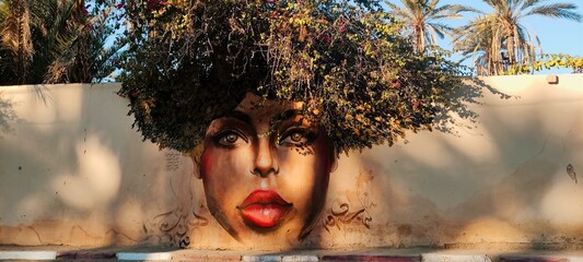 Graffiti drawn girl on the fence wall. Bushes of plants instead of girl's hair