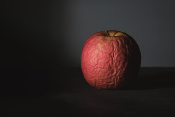 Aging of the surface. Withered skin of a rotten apple with a dark background. Old fruit dehydrated. The concept of life and death. Low key still life.