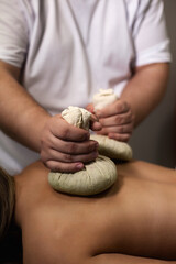 Masseur doing spa massaging of back with herbal compresses bag Thai method. Close up of relaxing...