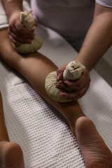 Masseur doing spa massage of leg with herbal compresses bag Thai method. Close up of relaxing...