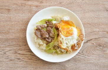 spicy stir fried slice beef meat with long sweet chili and onion on rice topping egg in plate 