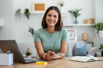 Beautiful business woman working with laptop while looking at camera in living room at home.