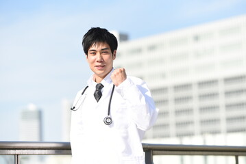 屋外でガッツポーズをする白衣を着た医療従事者のアジア人男性