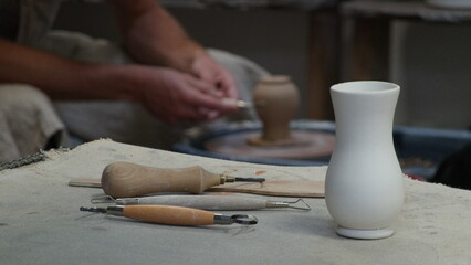 Fototapeta na wymiar The sculptor at work. White Vase on Table. Potter's tools. Potter's hands on a Background.