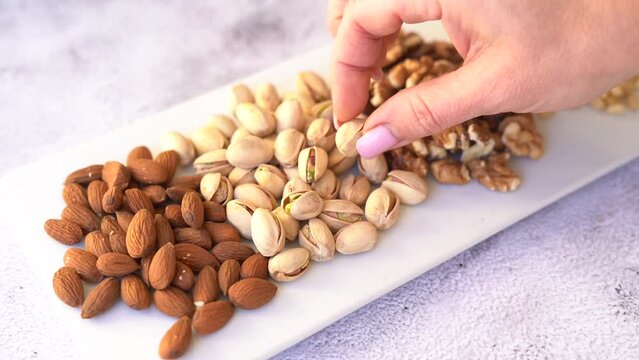 Mix of different nuts on a white plate. A woman's hand takes a nut.